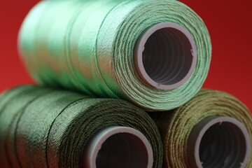 Spools of colorful sewing threads on red background, closeup