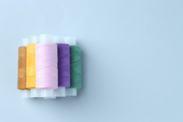Spools of colorful sewing threads on light background, top view. Space for text