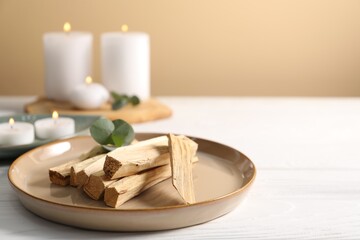 Palo santo sticks and eucalyptus leaves on white wooden table, closeup. Space for text