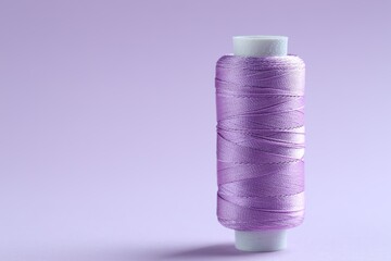 Spool of violet sewing thread on lilac background, space for text