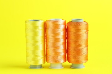 Spools of colorful sewing threads on yellow background