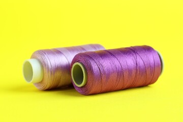 Spools of colorful sewing threads on yellow background, closeup