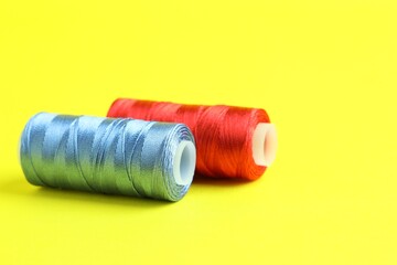 Spools of colorful sewing threads on yellow background, closeup. Space for text