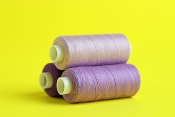 Spools of colorful sewing threads on yellow background, closeup