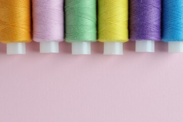 Spools of colorful sewing threads on pink background, flat lay. Space for text