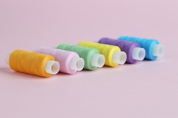 Spools of colorful sewing threads on pink background, closeup