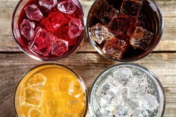 Soda water of different flavors with ice cubes in glasses on wooden table, flat lay