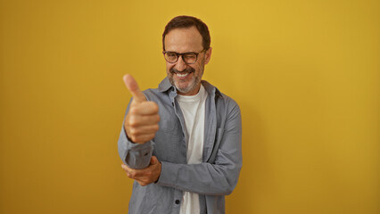 Handsome middle-aged hispanic man smiling and winking with thumbs up, isolated on yellow background