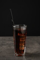 Cold cola with ice cubes and drinking straw in glass on grey table against black background. Space for text
