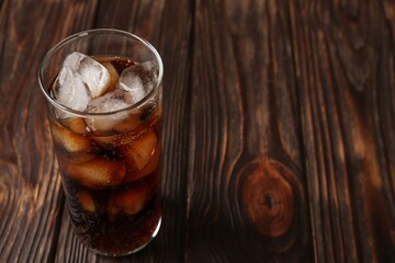 Cold cola with ice cubes in glass on wooden table. Space for text