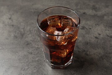 Cold cola with ice cubes in glass on grey table, closeup