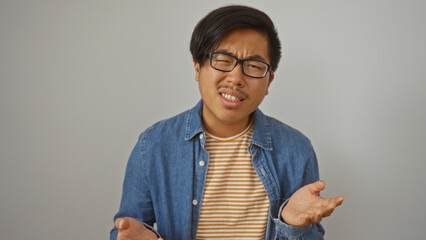 Handsome young man with glasses wearing striped shirt and denim jacket gestures in confusion...