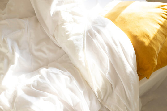 View of bed with sheets, duvet, pillow and cushions with soft sunlight