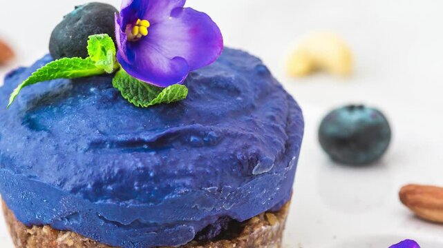 Blueberry and butterfly pea flower vegan cashew cheesecake with fresh berries, edible flowers, mint, nuts. Healthy vegan food concept. Tasty blue cake. Close up
