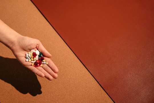 Woman's hand holding colorful pills over brown table.