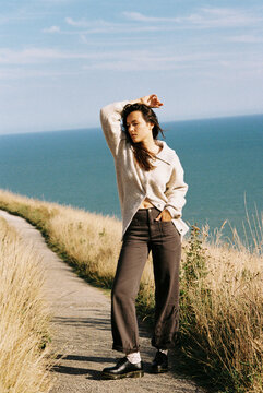 A woman in a cozy outfit standing on a trail overlooking the sea