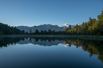 Fototapeta premium Hiking through lush native bush pedestrian footpath around the lakeside of Lake Matheson