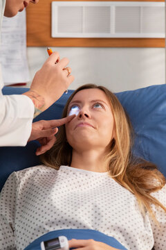 Doctor examining patient's eyes with light pen in hospital bed