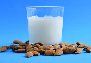 Almond milk, scattered natural almonds and milk in a glass, on a blue background.
