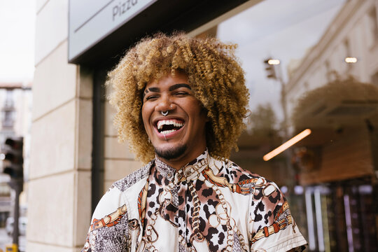 Smiling gay man with curly hair outside a city building