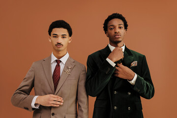 Two men adjusting suits and ties in front of brown backdrop