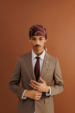 Stylish businessman wearing durag and suit posing on brown background