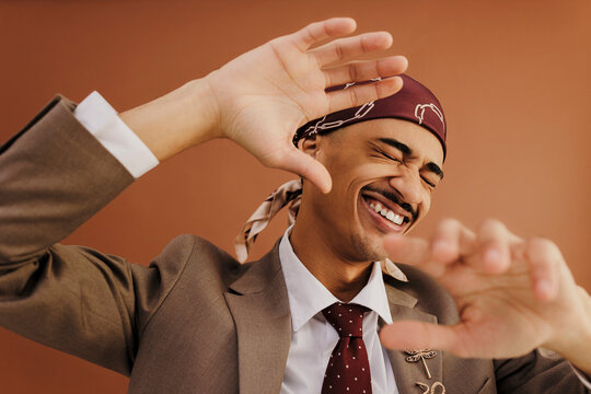 Playful man wearing durag and suit is gesturing and smiling in studio