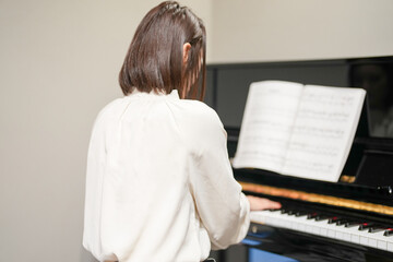 A Japanese woman in her 30s is playing the piano at home.
