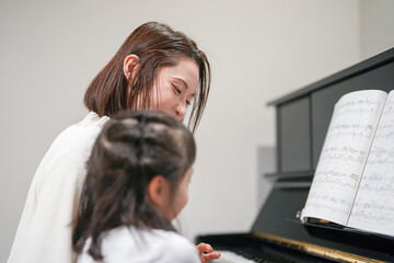A Japanese parent and child, a woman in her 30s and a 6-year-old girl, are playing the piano at...