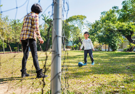 Child Playing Soccer in a Park with Mother Supervision
