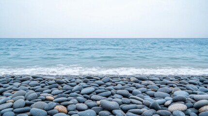 Tranquil Coastal Scene with Smooth Pebbles on Shoreline Against Calm Blue Ocean and Overcast Sky
