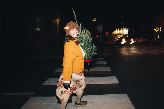 Woman Crossing Street at Night with a Christmas Tree