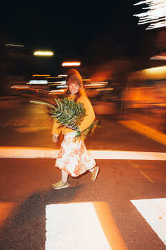 Woman with a Christmas Tree Crossing Street at Night