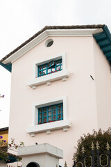 A cream-rose colored building with a triangular roof and two square windows. The simple, yet...