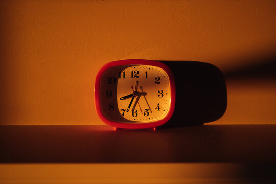 Vintage red alarm clock casts warm glow in morning light.