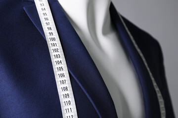 Male mannequin with blue jacket and measuring tape on grey background, closeup