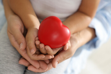 Little girl and her mother with red heart figure indoors, closeup