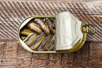 Tasty sprats in tin can on wooden table, top view