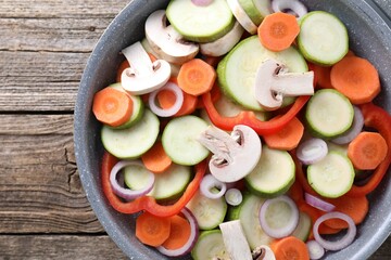 Frying pan with mix of fresh vegetables and mushrooms on wooden table, top view