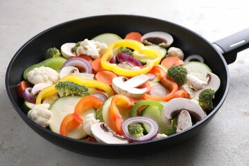 Frying pan with mix of vegetables and mushrooms on light grey table, closeup