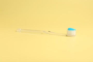 Toothbrush with toothpaste on yellow background, closeup