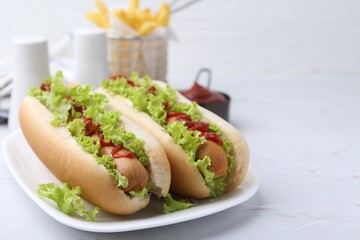 Tasty hot dogs with lettuce and ketchup on white table, closeup. Space for text