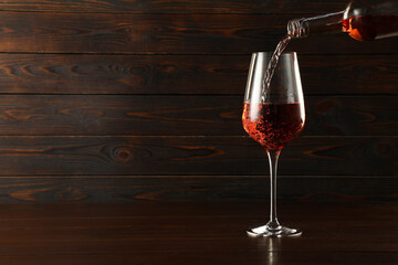Pouring rose wine into glass at wooden table, space for text