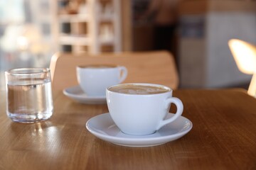 Cups of aromatic coffee and glass with water on wooden table in cafe, closeup
