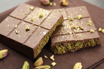 Pieces of tasty Dubai chocolate bar with pistachios and knafeh on table, closeup