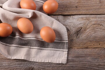 Many fresh eggs and towel on wooden table, flat lay. Space for text