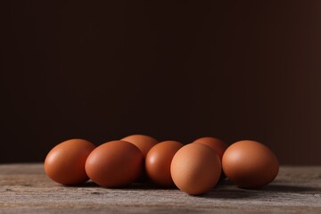 Fresh eggs on wooden table against brown background, closeup. Space for text