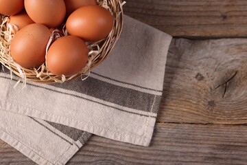 Wicker basket with fresh eggs on wooden table, top view. Space for text