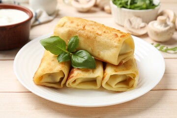 Delicious rolled crepes with basil, mushrooms and sour cream on wooden table, closeup