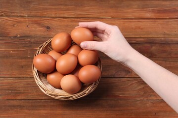 Woman with raw eggs at wooden table, top view